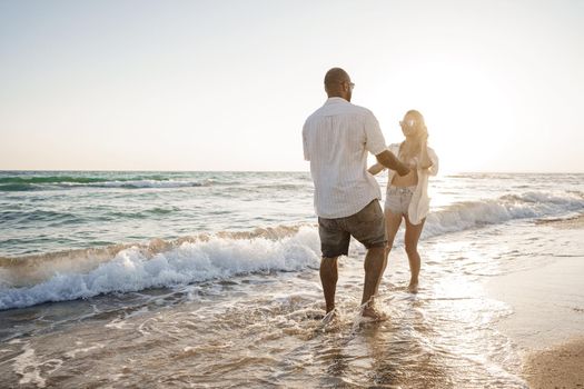 Young beautiful couple walking on beach near sea at sunset