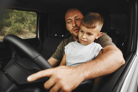 Father teaches little son to drive on road trip, close up