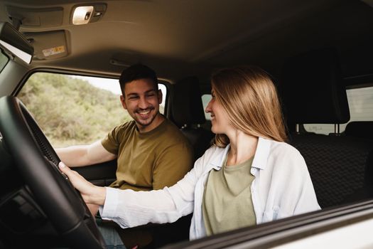 Beautiful young smiling couple sitting on front passenger seats and driving a car