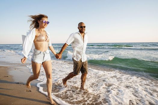 Young beautiful couple walking on beach near sea at sunset