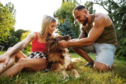 Young happy couple playing with their dog smiling in park, close up