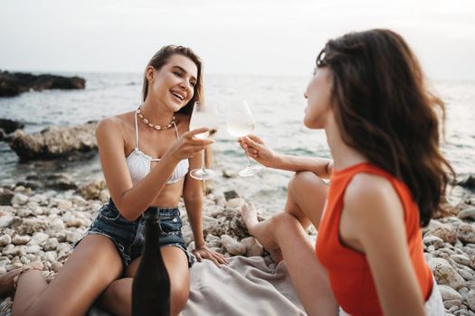 Two young female friends having a picnic on a beach drinking cocktails