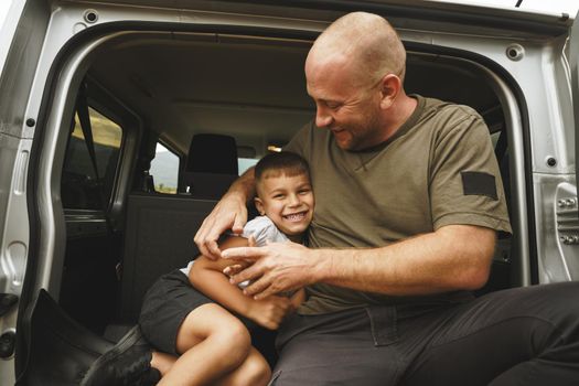 Happy father and son sitting in car trunk on road trip