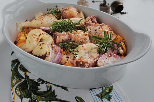 Chicken pieces prepared with pumpkin, onion, garlic and spices in a white ceramic baking dish. Decorated with rosemary. Autumn food concept