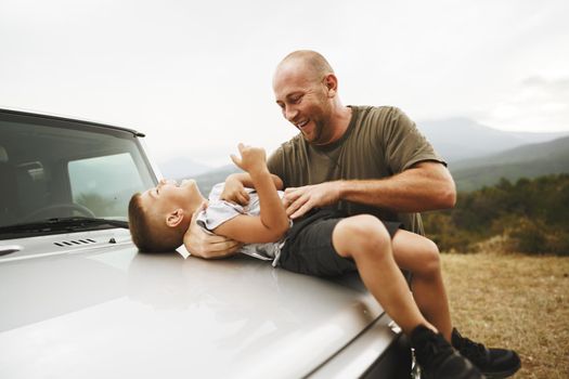 Dad and son playing on the hood of a car on road trip in mountains