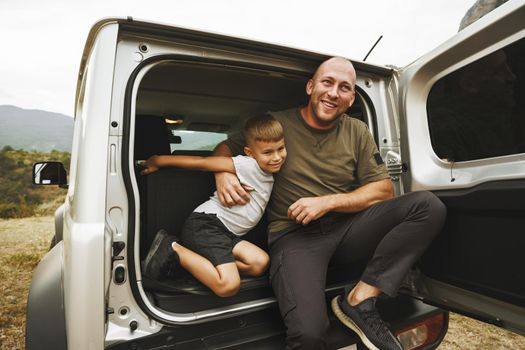 Happy father and son sitting in car trunk on road trip