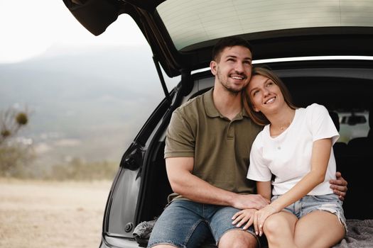 Young happy couple on a road trip sitting in car trunk outdoor