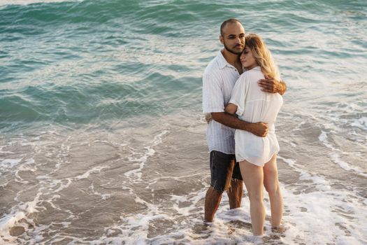 Beautiful young couple hugging on the beach by the water, close up