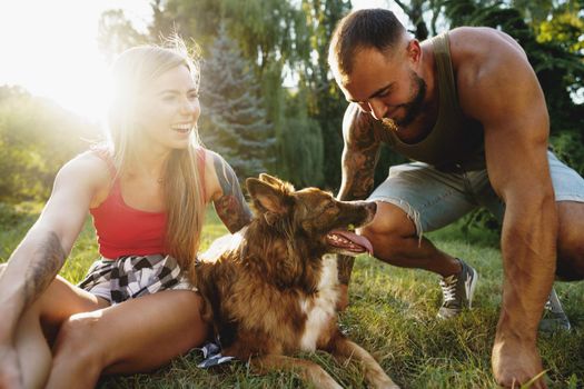 Young happy couple playing with their dog smiling in park, close up