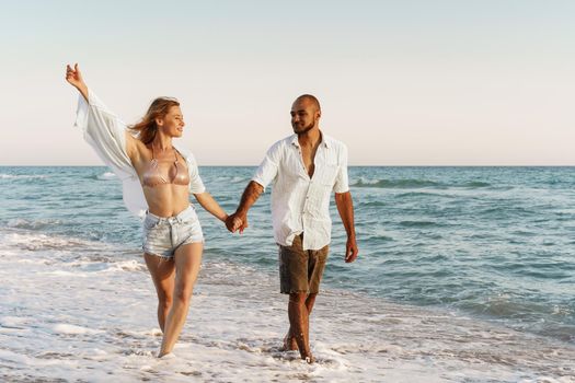 Young beautiful couple walking on beach near sea at sunset