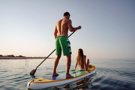 Couple of tourists young man and woman having fun paddleboarding at sea at sunset