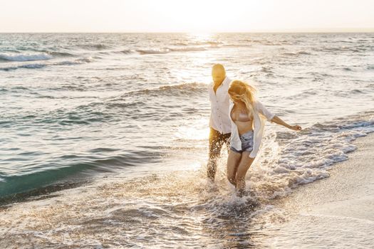 Young beautiful couple walking on beach near sea at sunset