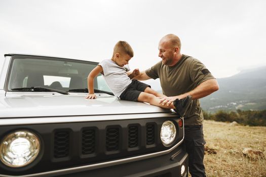 Dad and son playing on the hood of a car on road trip in mountains