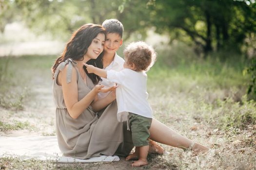 Happy young woman with children on wheat summer field. Happy motherhood. Adventure, travel, tourism, hike and people concept - happy family walking