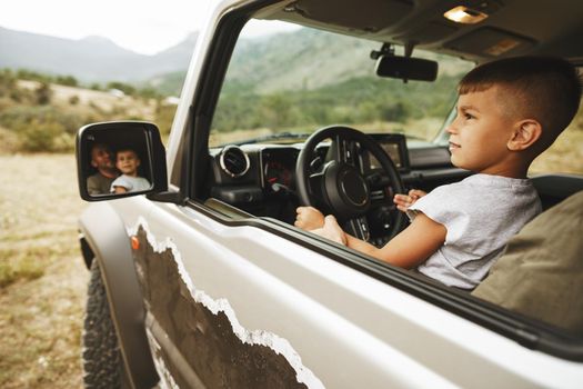 Father teaches little son to drive on road trip, close up