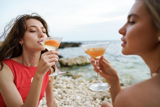 Two young female friends having a picnic on a beach drinking cocktails