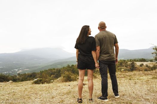 Back view of couple standing and looking at foggy mountains in autumn