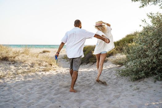 Young happy couple holding hands and walking together to the beach ocean on summer day