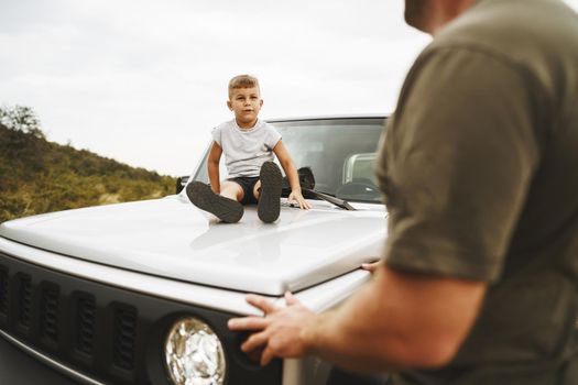 Dad and son playing on the hood of a car on road trip in mountains