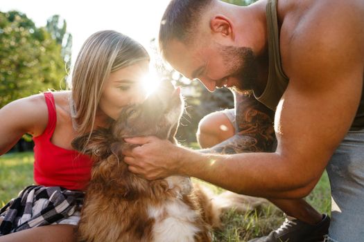 Young happy couple playing with their dog smiling in park, close up