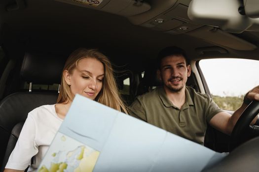 Young loving couple on a road trip using map inside a car, close up