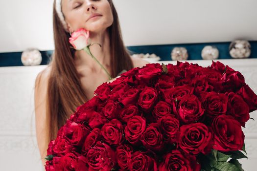 Close-up of bunch of stunning red roses and unrecognizable woman with flower in blurred background.