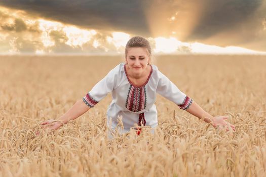 girl in an embroidered shirt on a wheat field and a sunset sky