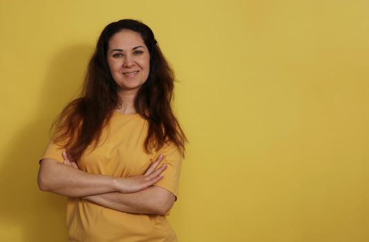 Beautiful woman in T-shirt standing on yellow isolated background with a slight smile on her face. A happy person. Pleasant brunette on a yellow background.