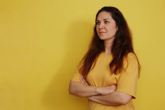 Beautiful woman in yellow t-shirt with long dark hair on yellow paper background. Pleasant brunette on a yellow background.