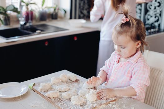 Happy wife smiling and preparing breakfast together with child for husband. Beautiful mother with cute daughter cooking in pajamas in morning. Little lovely kid helping parent with dough at kitchen.