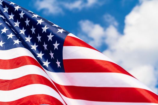 American flag on flagpole waving in the wind against white clouds