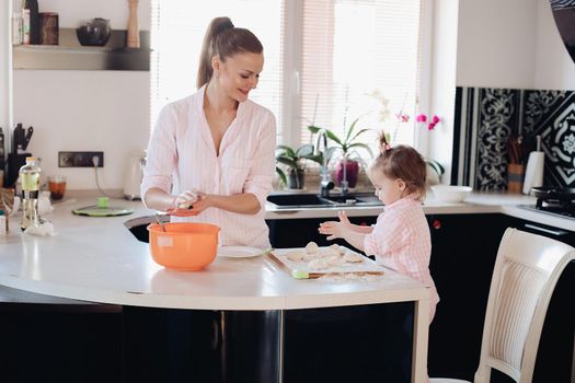 Happy wife smiling and preparing breakfast together with child for husband. Beautiful mother with cute daughter cooking in pajamas in morning. Little lovely kid helping parent with dough at kitchen.