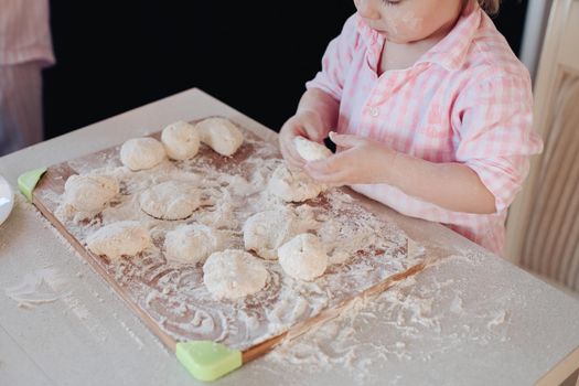 Happy wife smiling and preparing breakfast together with child for husband. Beautiful mother with cute daughter cooking in pajamas in morning. Little lovely kid helping parent with dough at kitchen.