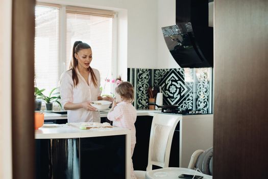 Lovely mother playing with little daughter in kitchen. Cheerful woman and cute girl cooking and baking donuts at kitchen. Happy family laughing and talking together at home. Concept of love and joy.