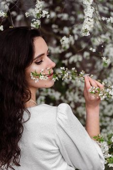 Girl touches and sniffs a branch of a white flowering tree without medical mask. Spring walking in the park