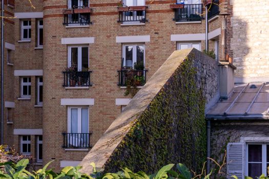 Parisian tenement brick house with flowers and greenery on the windowsills on a sunny day