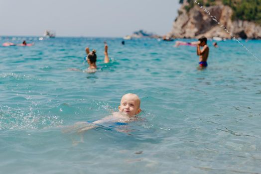 Child learning to swim in the open sea of tropical resort. Kids learn swimming. Exercise and training for young children. Little boy with colorful float board in sport club. Swimming baby or toddler. Happy child boy swims in sea in swimming circle with splash. Blue sky and water. Swimming training. Fun joy activities on vacation in the beach. Childhood moments lifestyle. Freedom careless. boy swim in the sea.