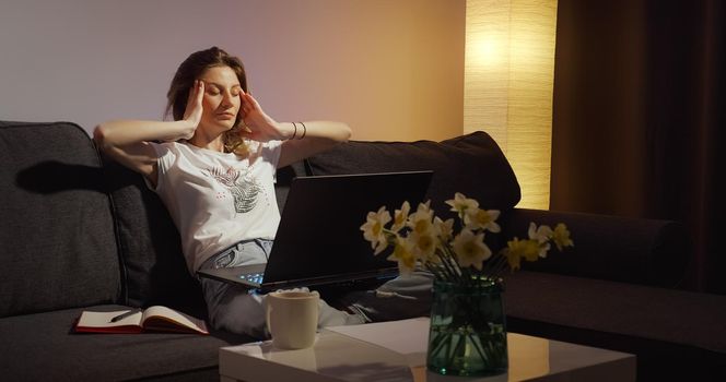 Young woman working on laptop alone in dark living late at night finishing urgent work overworking.