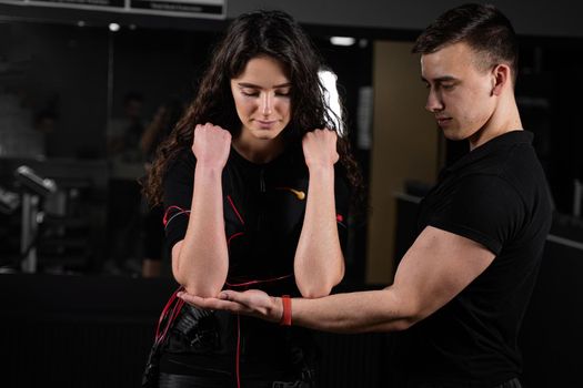 Man trainer trains a girl in an EMS suit in the gym. Electrical stimulation of the misc during active training.