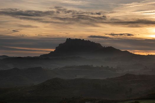 Landscape showing Montserrat mountain over the mist and under a cloudy sky in dawn