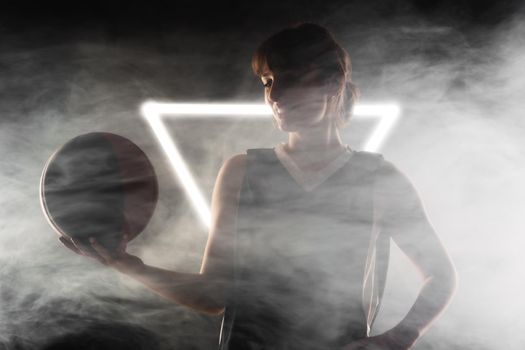 Beautiful girl with basketball. Side lit studio portrait against fog background with white neon lights.