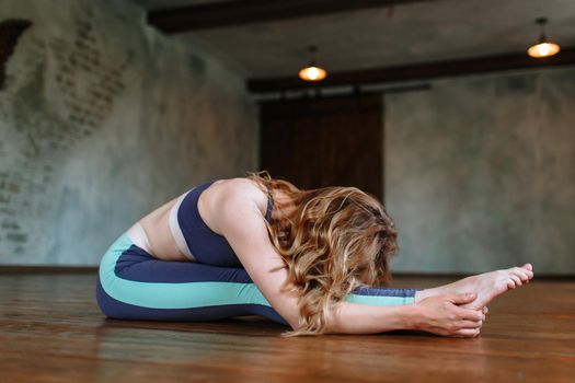 Yoga girl performs a difficult exercise in the loft. Paschimottanasana