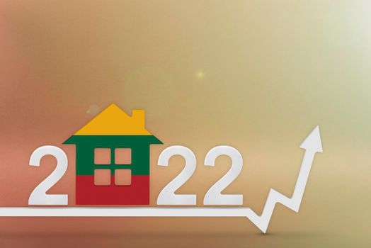 The cost of real estate in Lithuania in 2022. Rising cost of construction, insurance, rent in Lithuania. House model painted in flag colors, up arrow on yellow background.