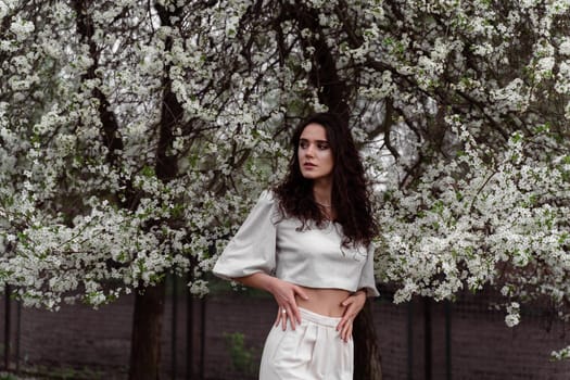 Portrait of young woman in the garden. Attractive girl weared white dress posing near blooming trees