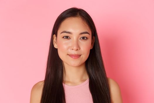 Beauty, fashion and lifestyle concept. Close-up of beautiful happy asian girl with perfect white smile, looking upbeat, standing hopeful and upbeat over pink background. Copy space