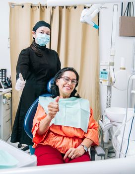 Dentist with thumb up patient in office, Woman shows thumb up sitting in dentist office, Dentist and satisfied patient with thumb up