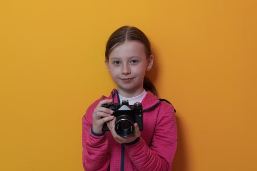 Little girl photographer isolated on yellow background smiling taking photos with a retro vintage camera. High quality photo