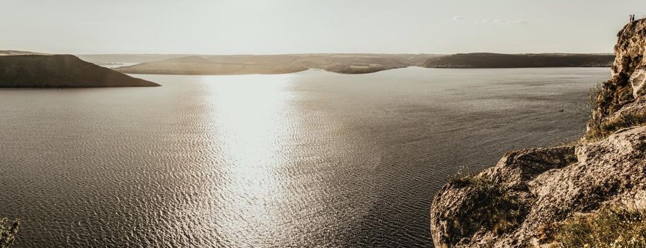 Panoramic view A couple of people in love, a man and a woman, stand on the Big Mountain above the cliff over the sea with islands at sunset. View from a drone on a huge stone rock.