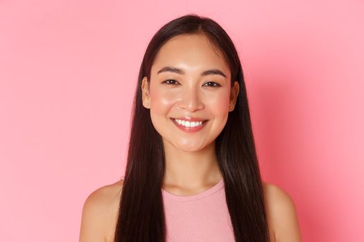 Beauty, fashion and lifestyle concept. Close-up of beautiful happy asian girl with perfect white smile, looking upbeat, standing hopeful and upbeat over pink background. Copy space