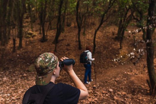 two friends climbing to the top of a mountain. young women on vacation. women using binoculars,bird watching. hiking sticks and mountaineer's backpack. warm, natural light. lush vegetation. hiking sticks.